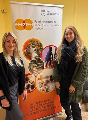 Zwei Mitarbeiterinnen neben einem Plakat-Austeller des effzett Familienzentrums