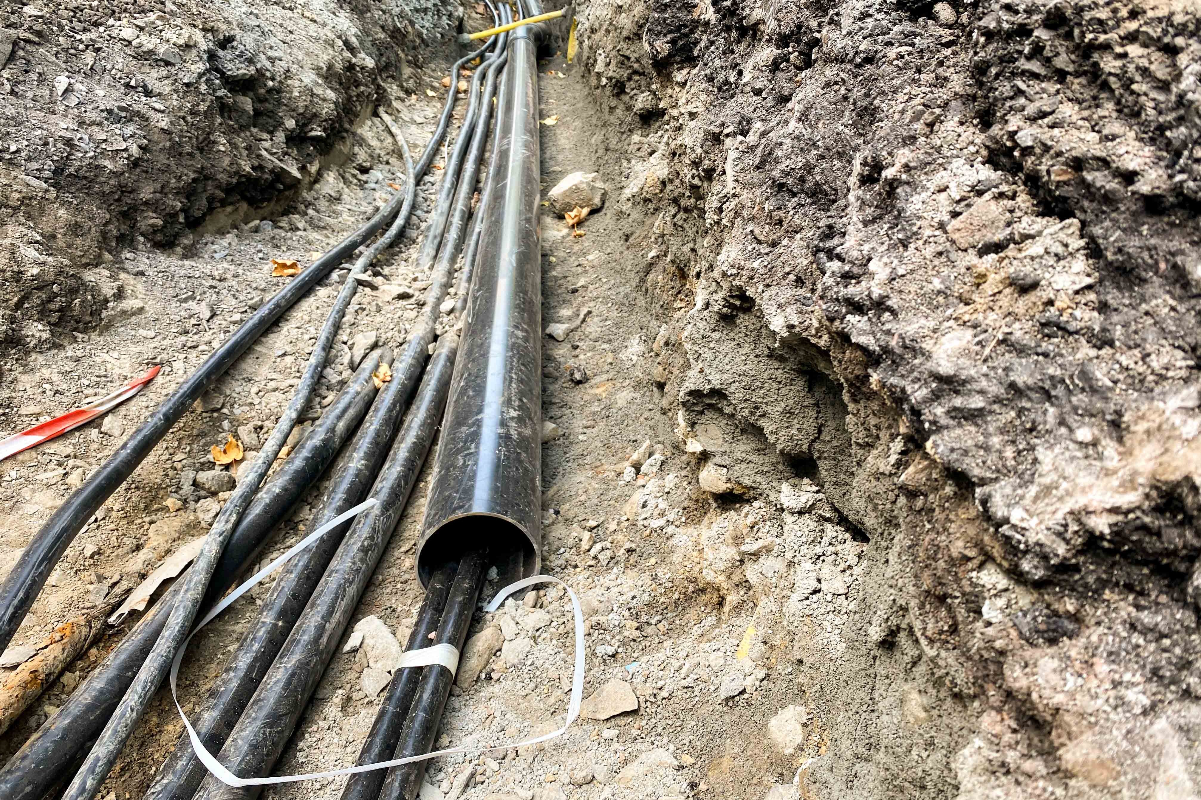 In einer aufgerissenen Straße werden Leerrohre verlegt.