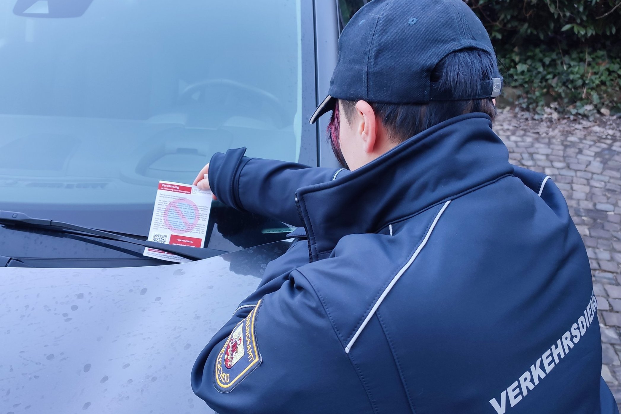 Ein Mitarbeiter des Ordnungsamtes heftet ein Knöllchen an die Windschutzscheibe