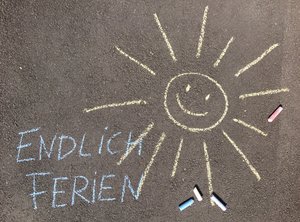 Eine Sommer und "Endlich Ferien" ist mit bunter Kreide auf die Straße gemalt