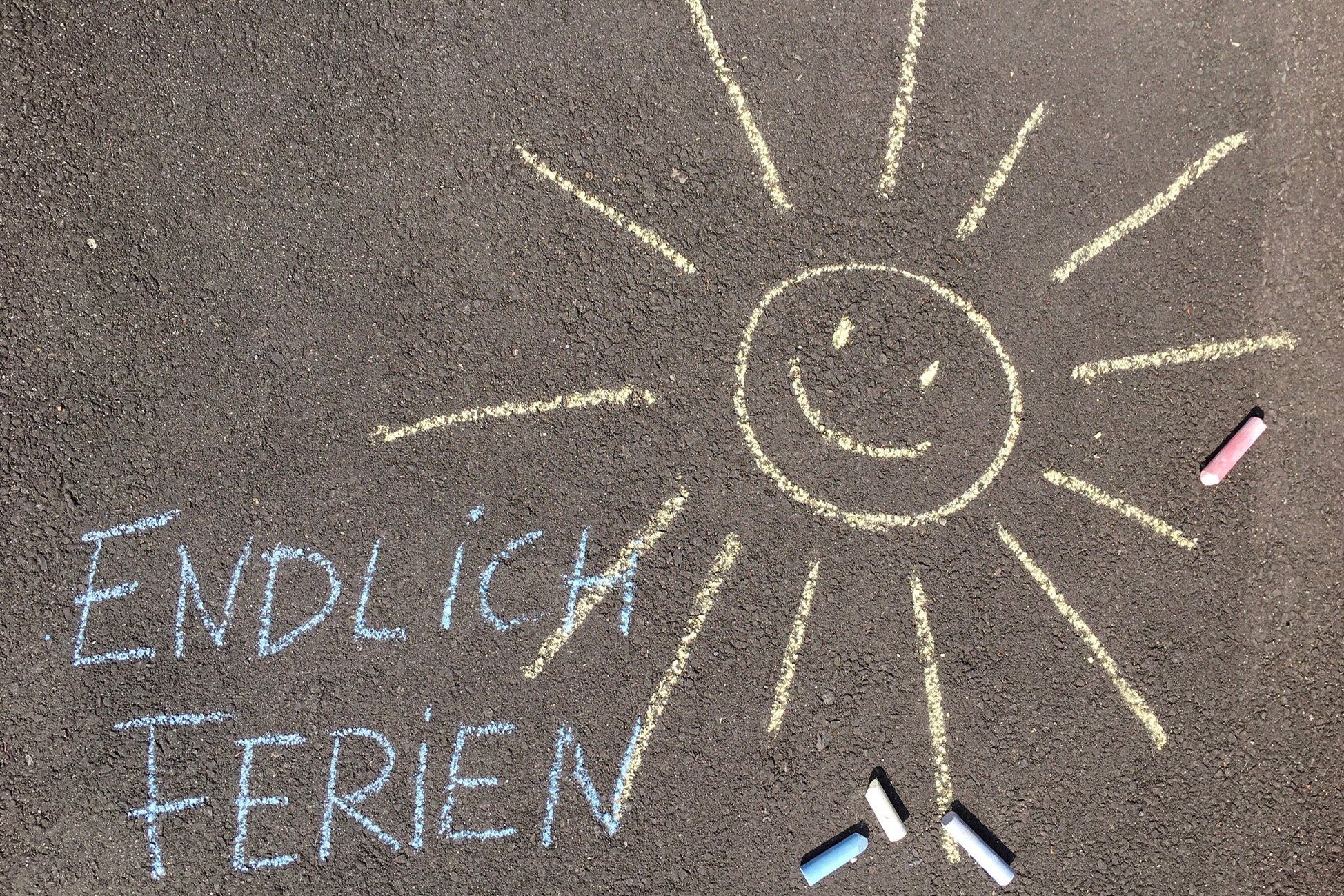 Eine Sommer und "Endlich Ferien" ist mit bunter Kreide auf die Straße gemalt