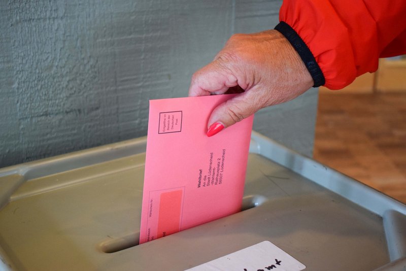 Eine Frau wirft einen roten Briefwahlumschlag in die Wahlurne