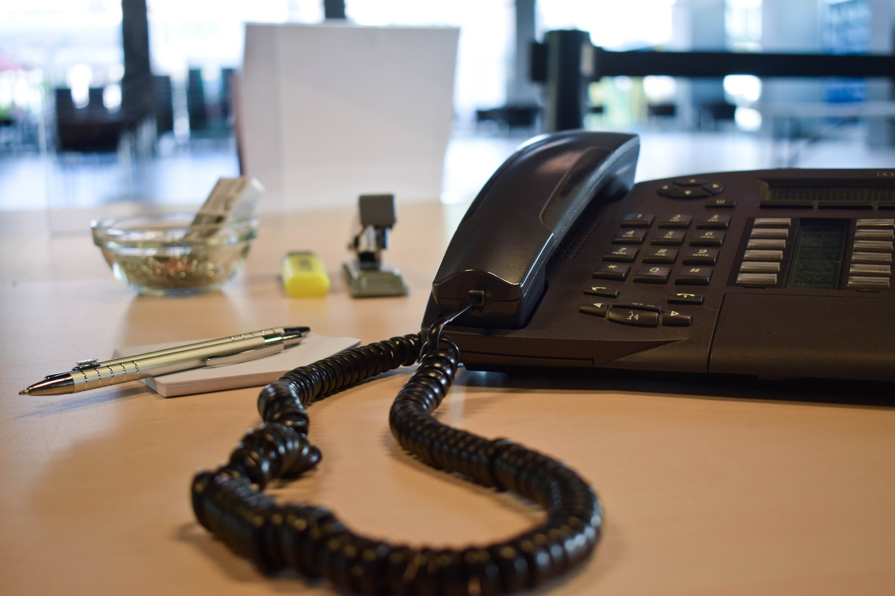 Ein Telefon steht auf einem Schreibtisch, auf dem außerdem Büromaterialien zu sehen sind.