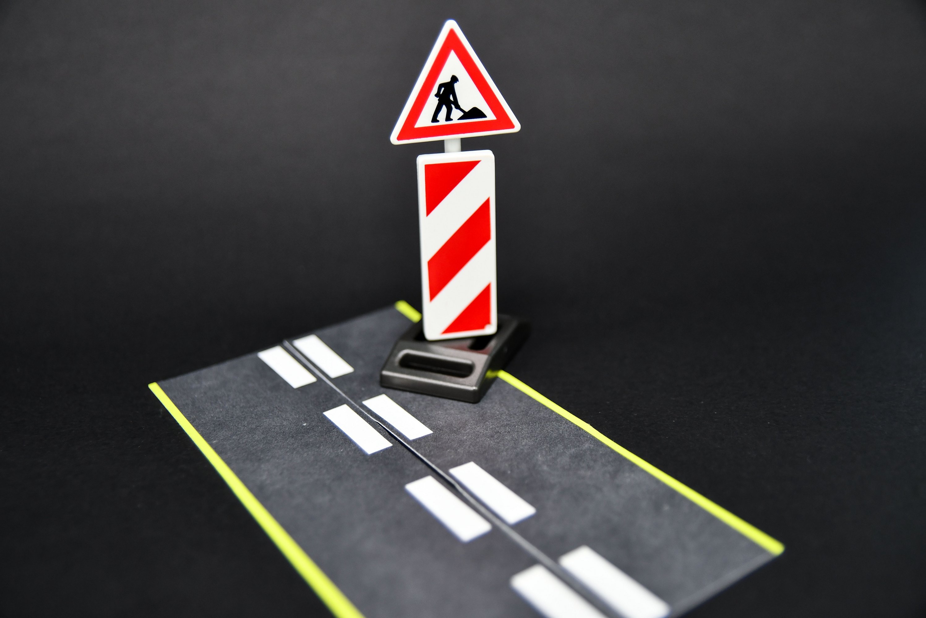 Ein Stück Straße, auf der eine Baustellenbake und ein Baustellenschild aufgebaut sind.