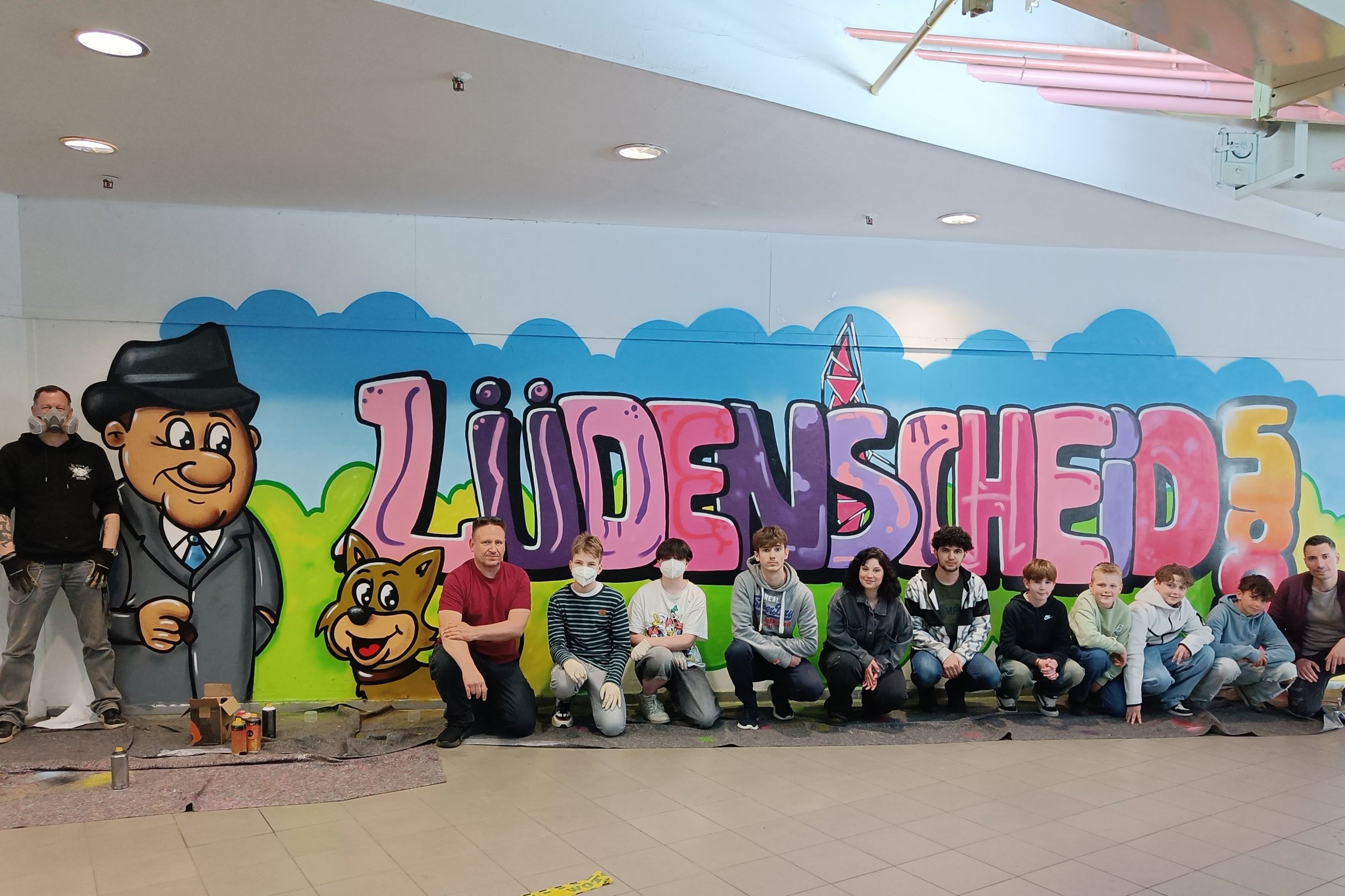 Eine Gruppe Jugendlicher vor einem Graffiti mit Lüdenscheider Motiven im Forum am Sternplatz.