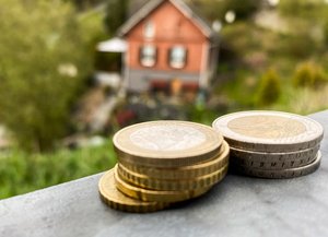 Kleine Stapel Geldmünzen, im Hintergrund ein Haus mit Garten