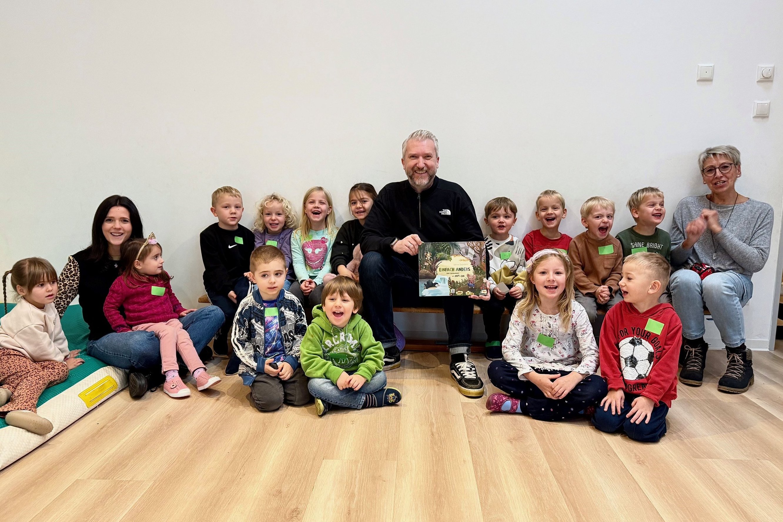 Bürgermeister Sebastian Wagemeyer sitzt mit mehreren Kita-Kindern und zwei Erzieherinnen auf einer Bank. 