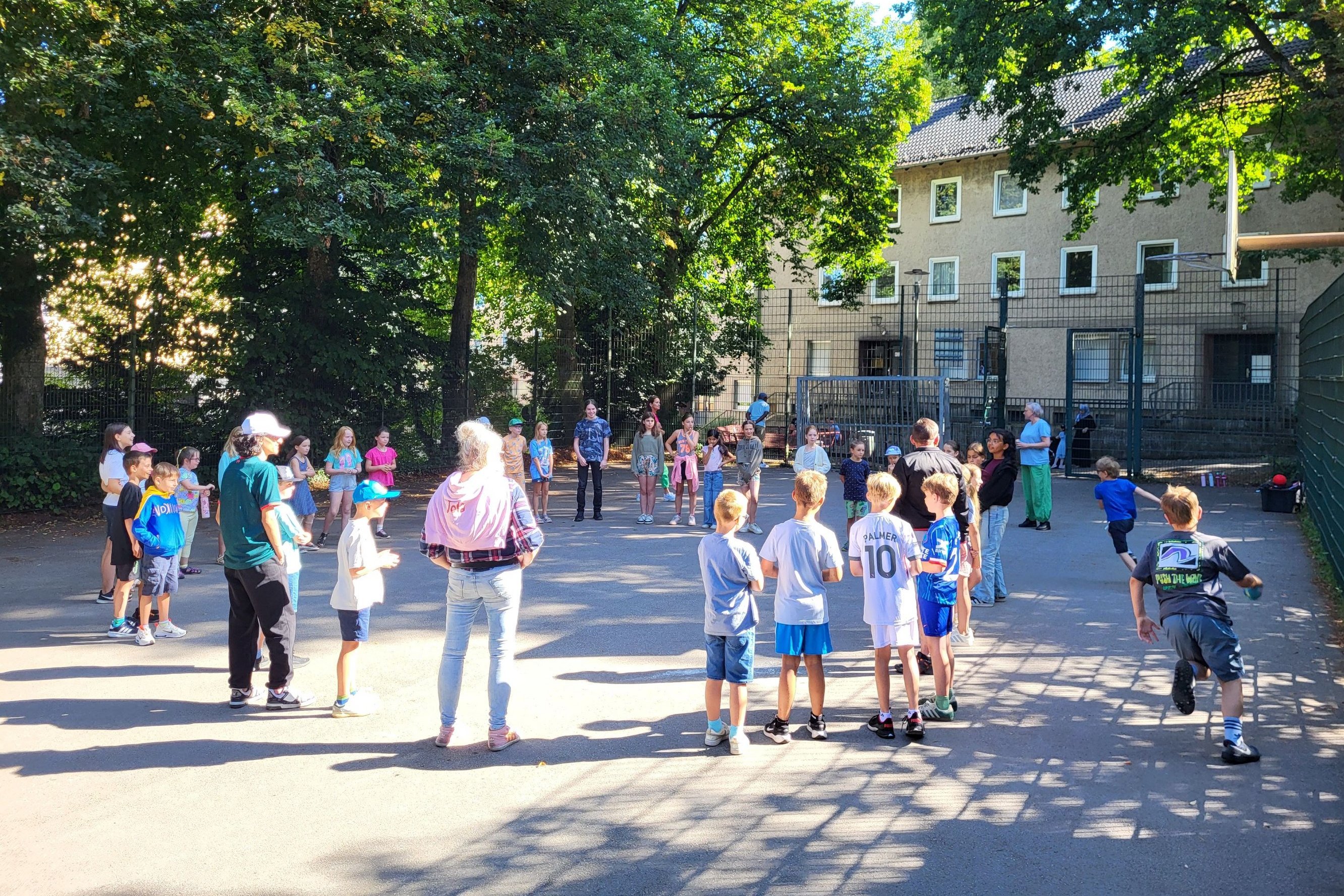 Kinder stehen in einem Spielkreis auf einem Platz.