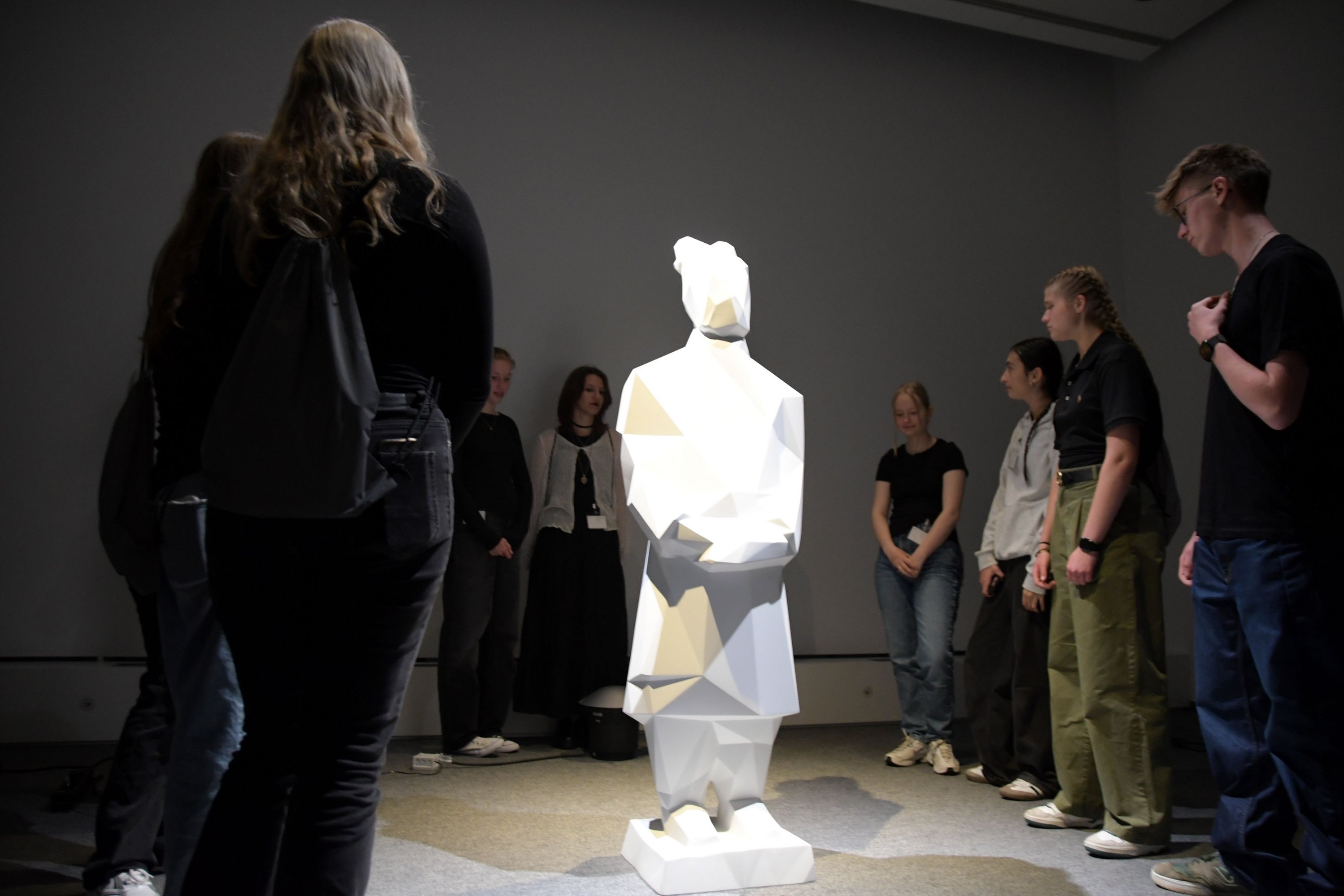 Eine Schülergruppe steht im Halbkreis um eine beleuchtete Skulptur herum