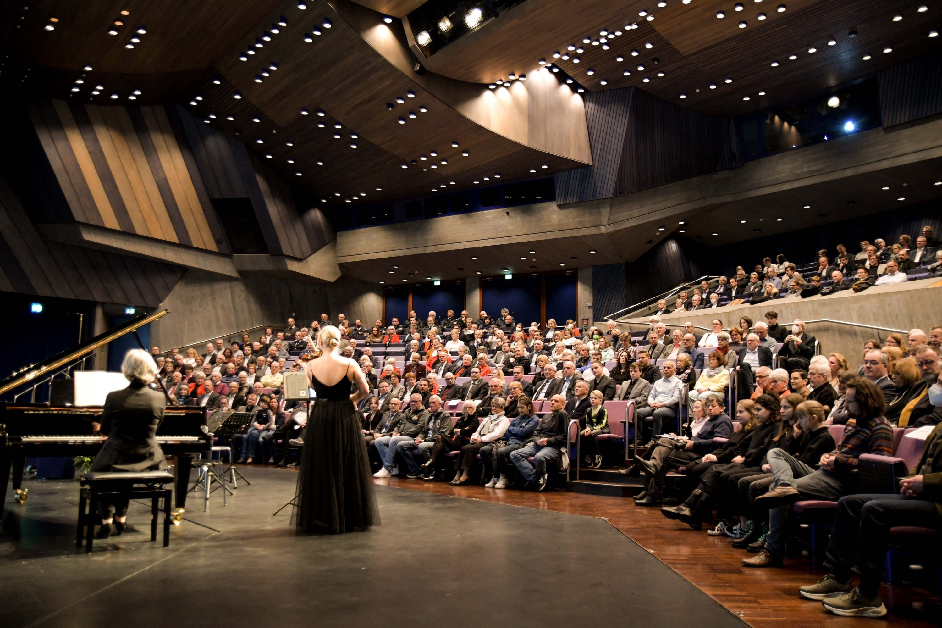 Eine Violinistin spielt ihr Instrument in einem voll besetzten Theatersaal.