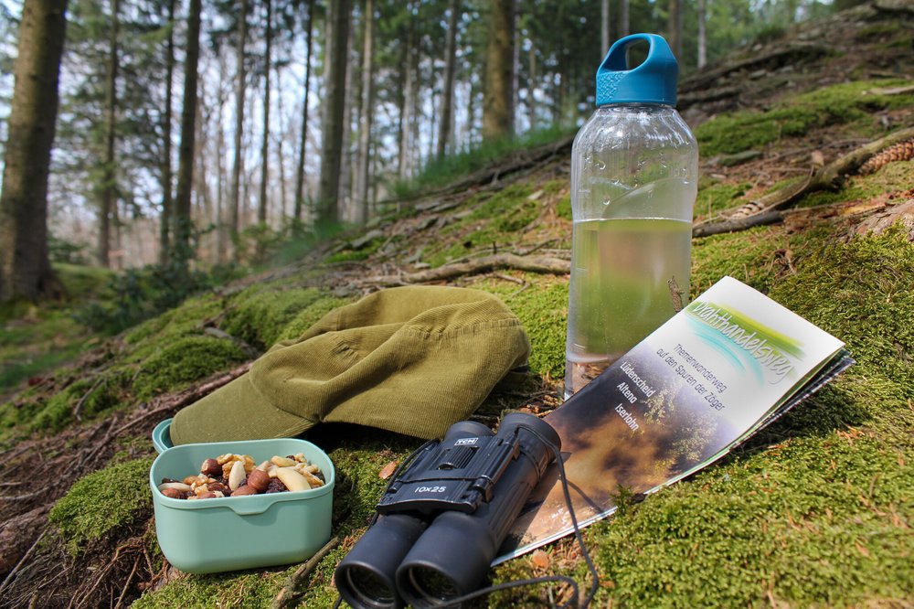 Waldboden mit Proviantdose, Trinkflasche, Schirmmütze, Fernglas und Wanderkarte