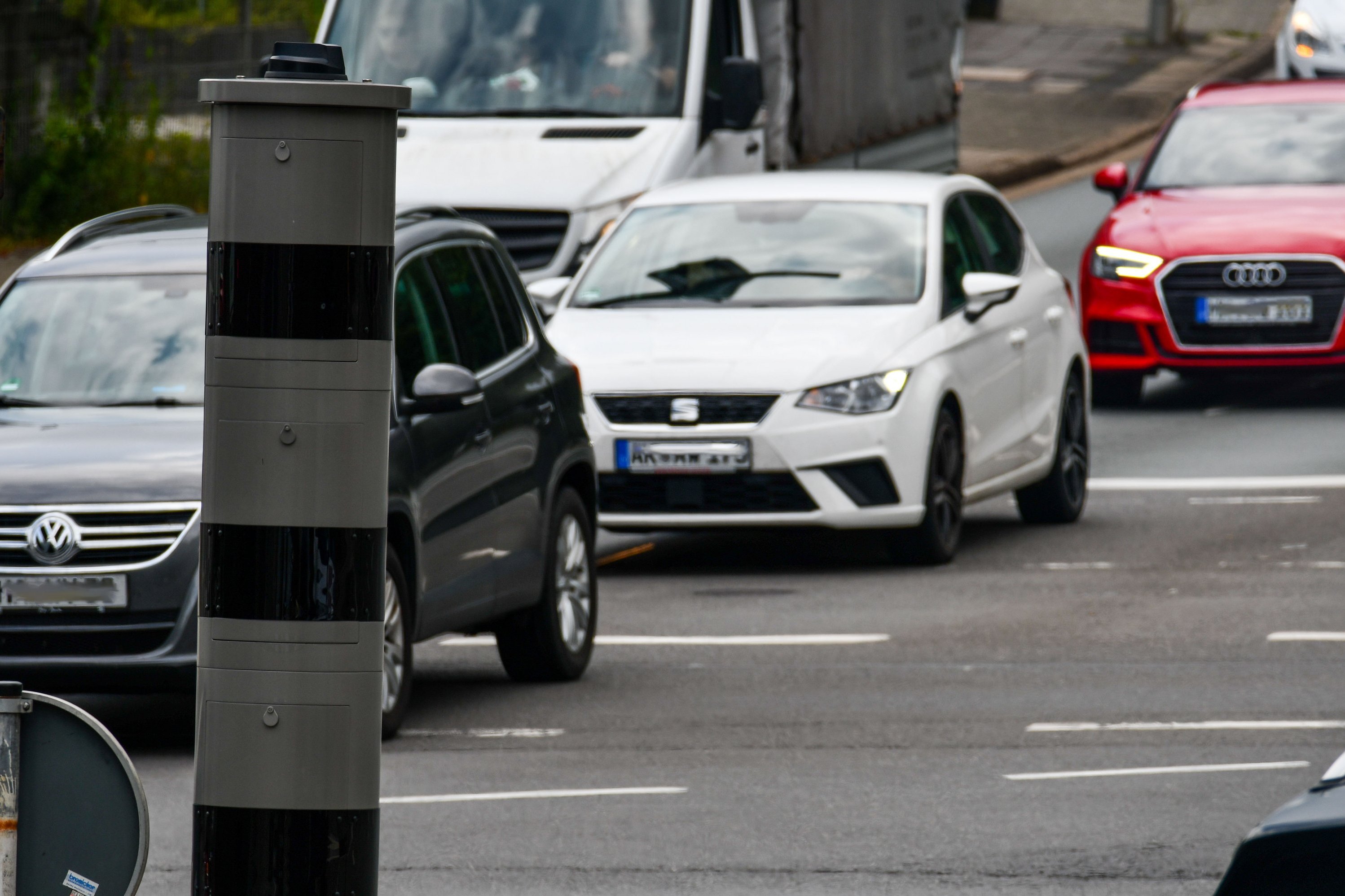 Autos befahren eine Straße. Im Vordergrund steht ein Rotlichtblitzer.