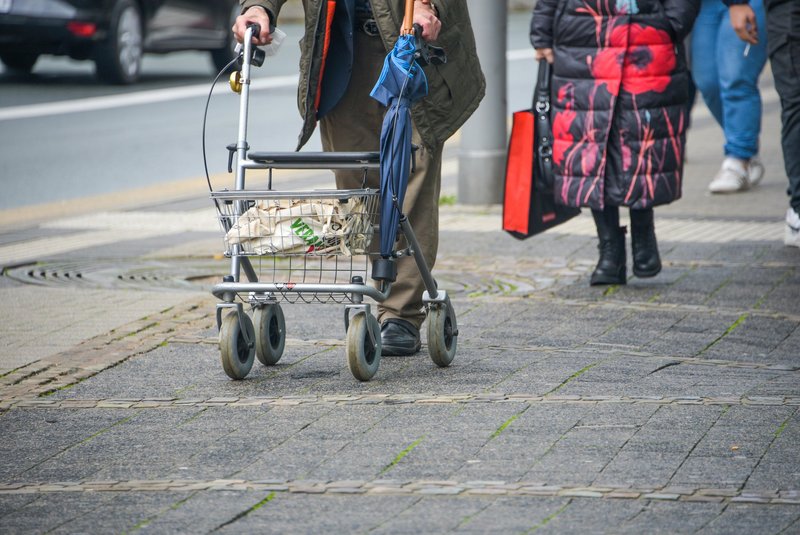 Passanten auf dem Gehweg, einer mit Rollator