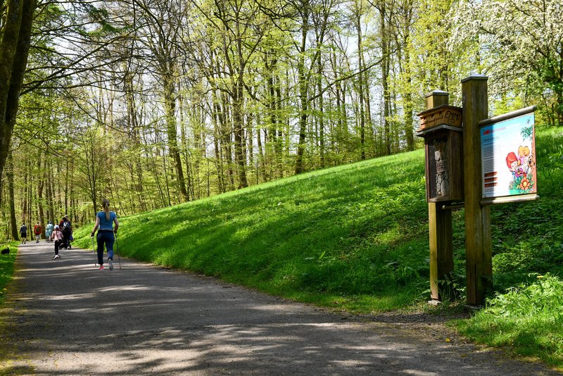 Wanderweg mit Tafel und Insektenhotel des Naturerlebnispfades, im Hintergrund Spaziergänger
