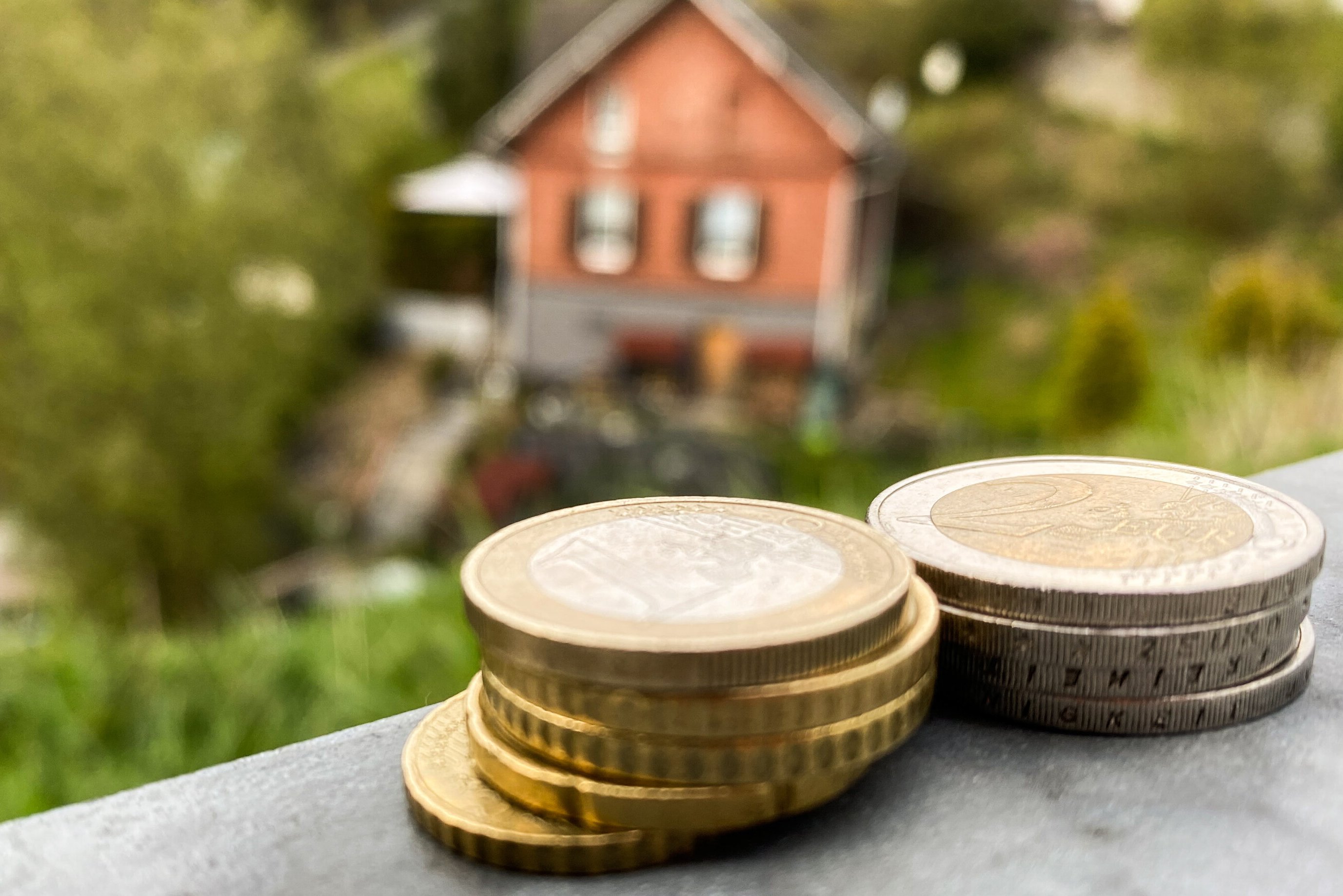 Zwei kleine Stapel Münzgeld mit einem Eigenheim im Hintergrund