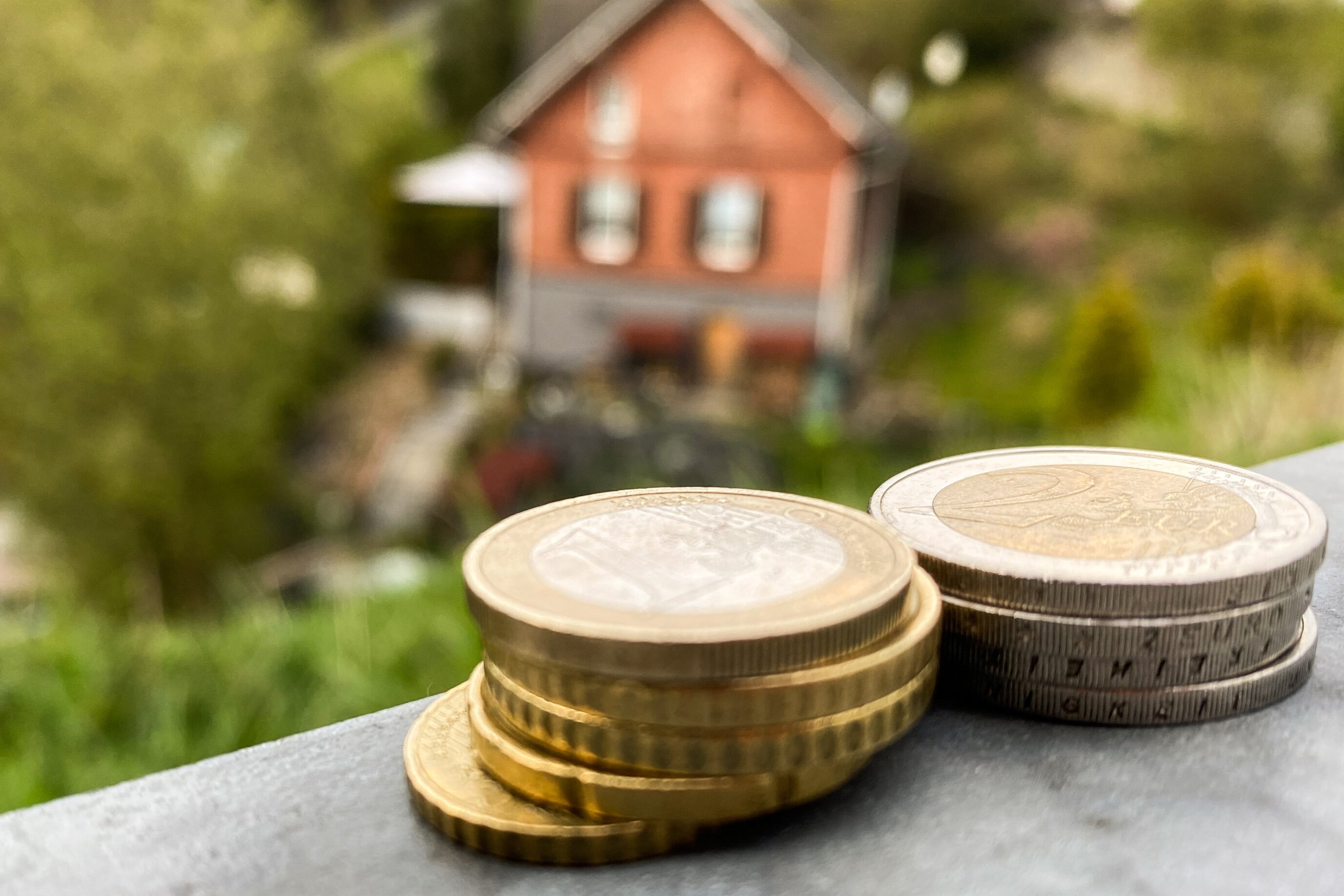 Zwei kleine Stapel Münzgeld mit einem Eigenheim im Hintergrund