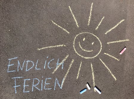 Mit bunter Kreide ist eine Sonne und "Endliche Ferien" auf die Straße gemalt