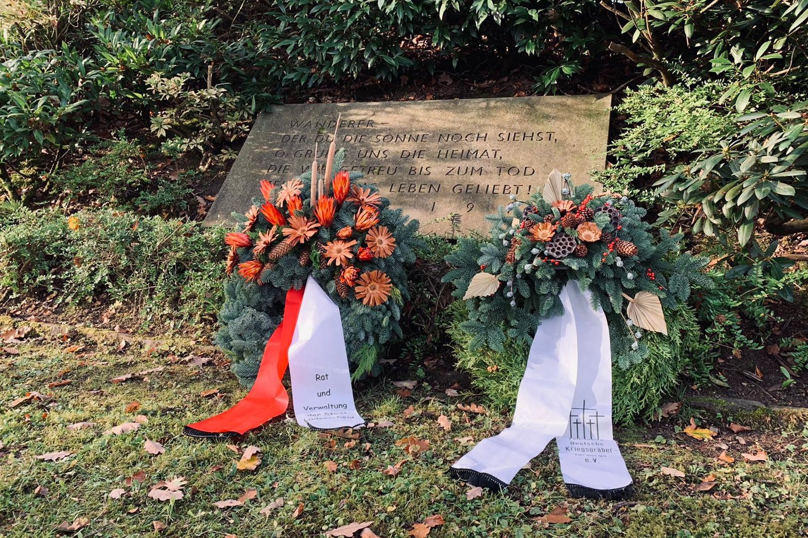 Zwei Kränze vor einer Gedenktafel.