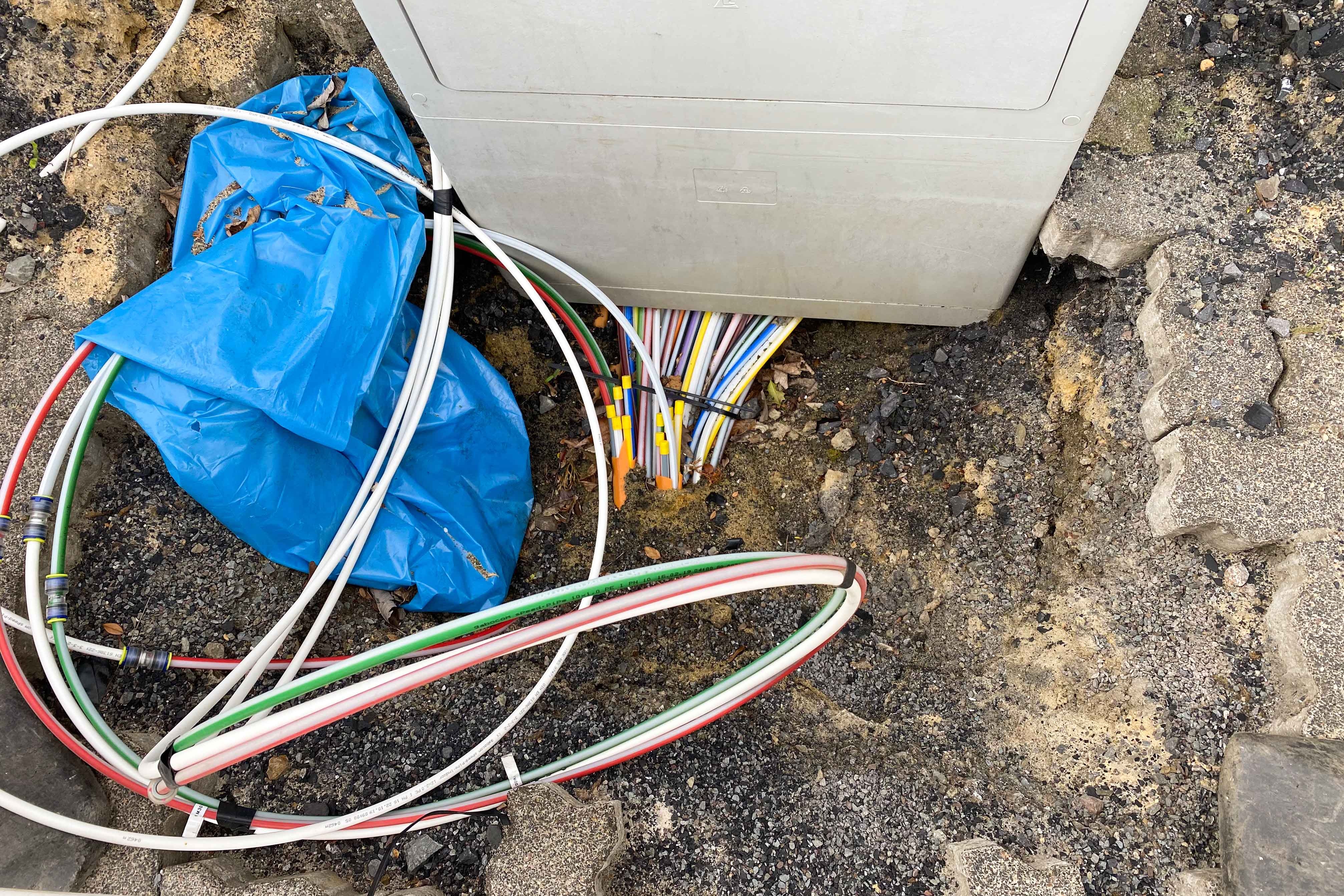 Kabel, die im Boden in einen Verteilerkasten münden.