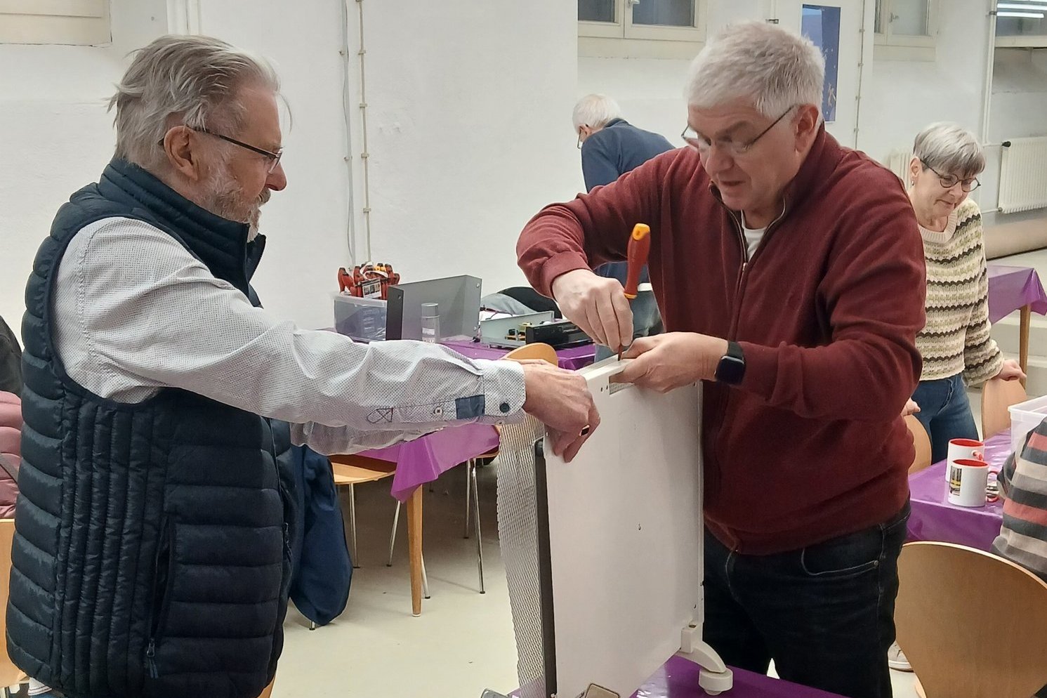 Zwei Männer reparieren einen defekten Gegenstand im Reparaturcafé