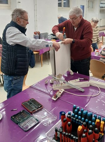 Zwei Männer reparieren einen defekten Gegenstand im Reparaturcafé