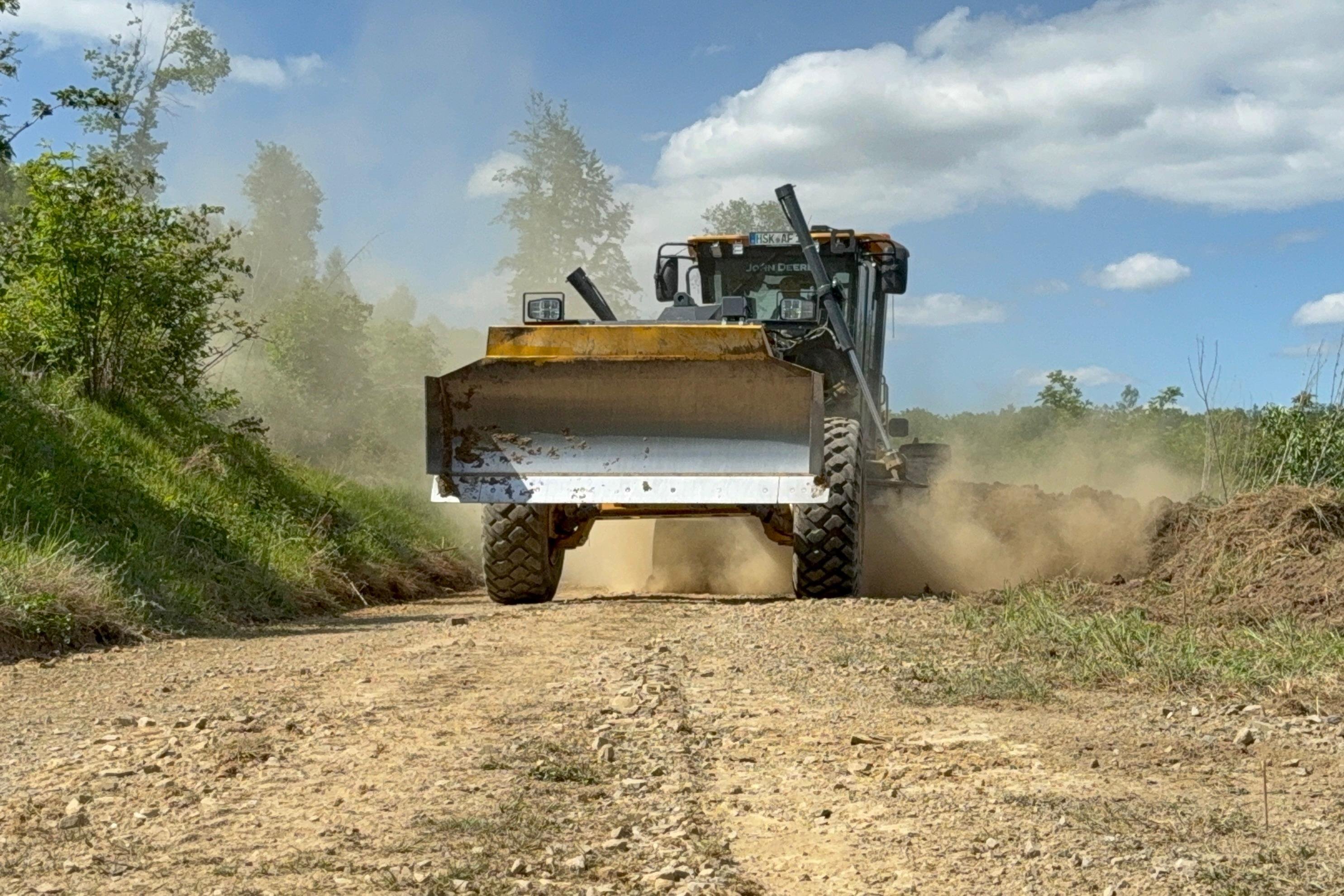 Ein Grader, eine Mischung aus Trecker und Planierraupe, fährt einen Forstweg entlang.