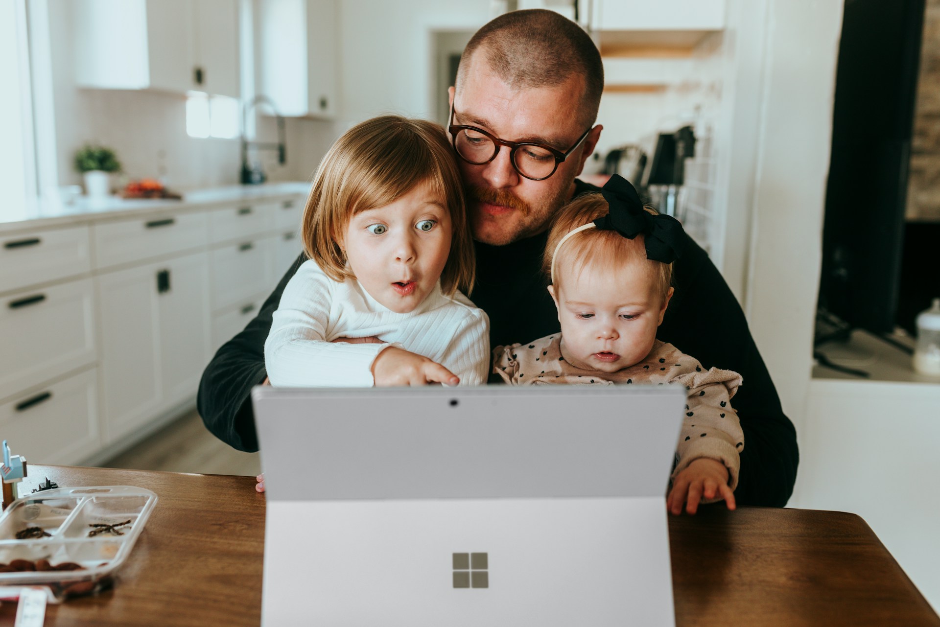 Vater sitz mit zwei kleinen Kindern auf dem Schoß vor einem Laptop
