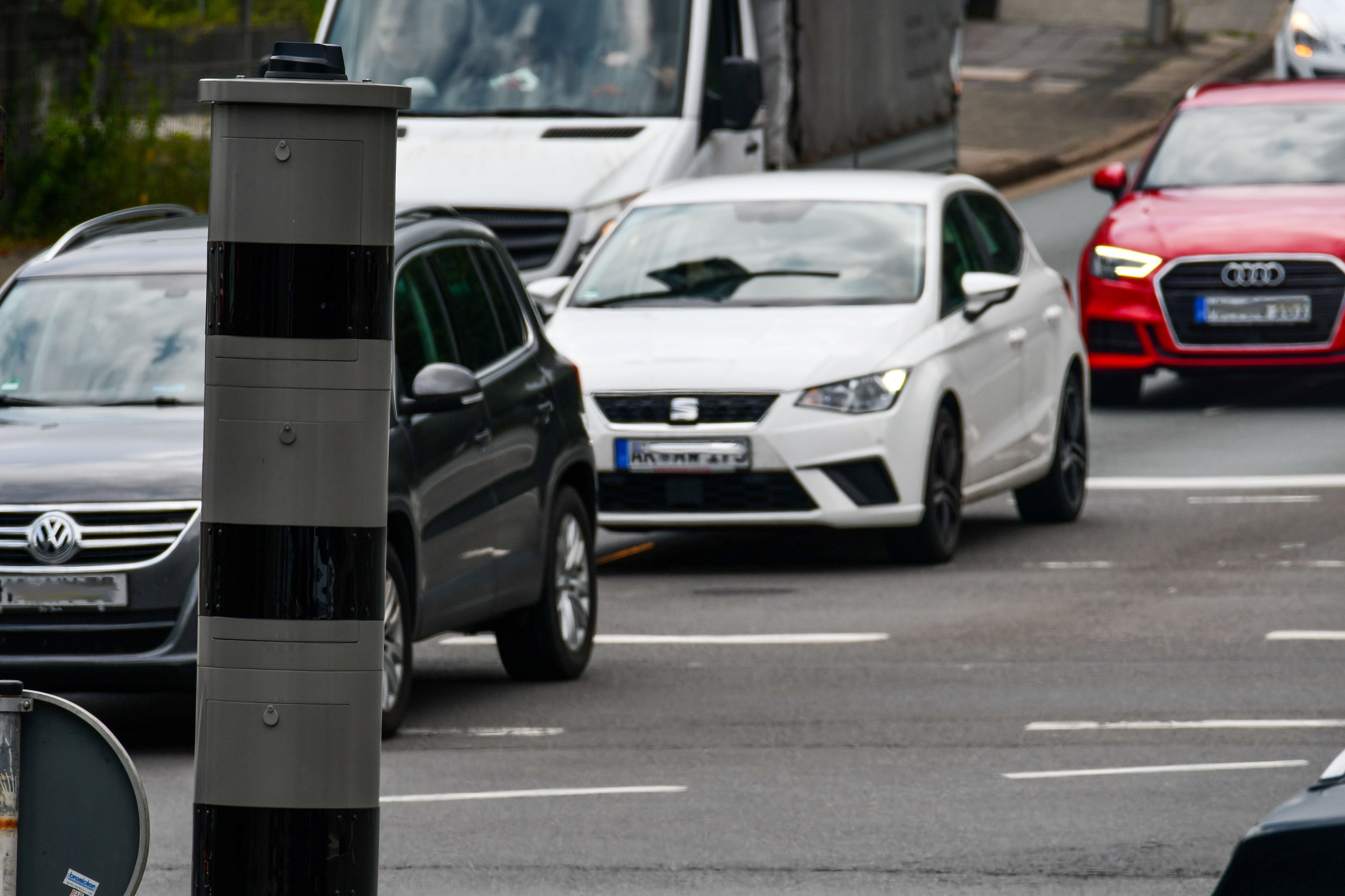 Autos befahren eine Straße. Im Vordergrund steht ein Rotlichtblitzer.