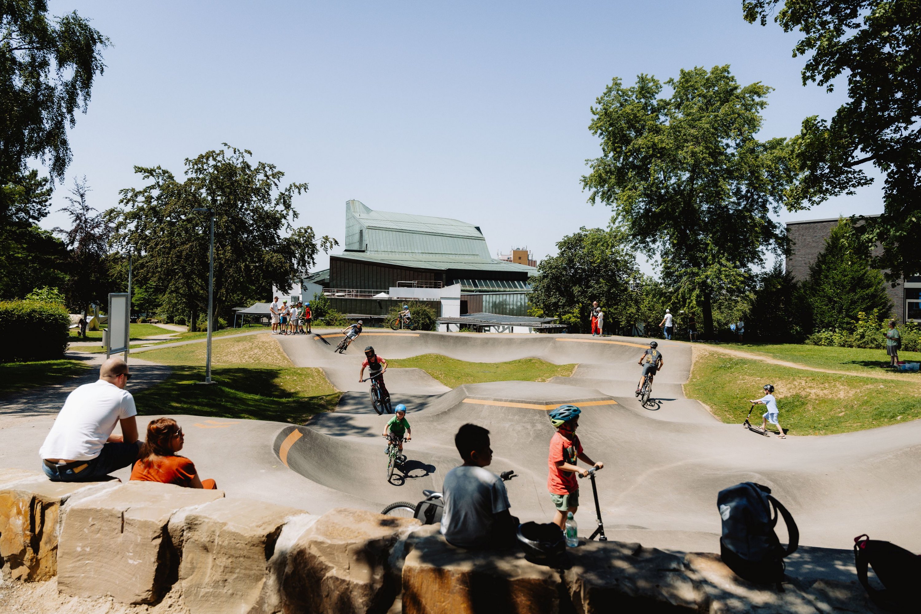 Kinder und Jugendliche befahren den Pumptrack im Stadtgarten mit Fahrrädern und Scootern.